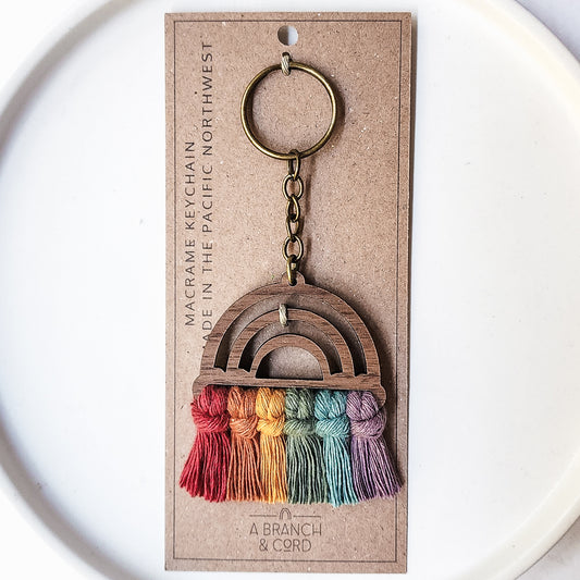 A wooden keychain with a rainbow pattern on a white background with a product tag.