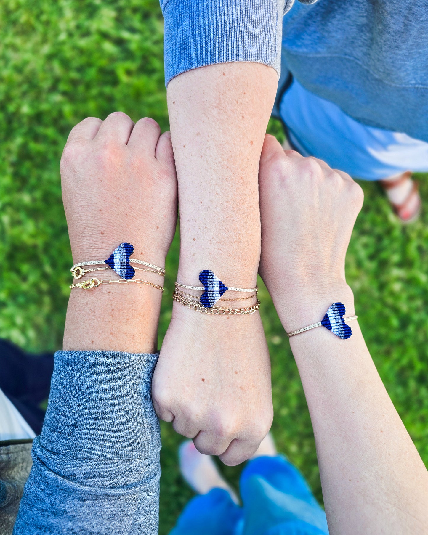 Three arms with blue heart-shaped bands on wrists against a grassy background