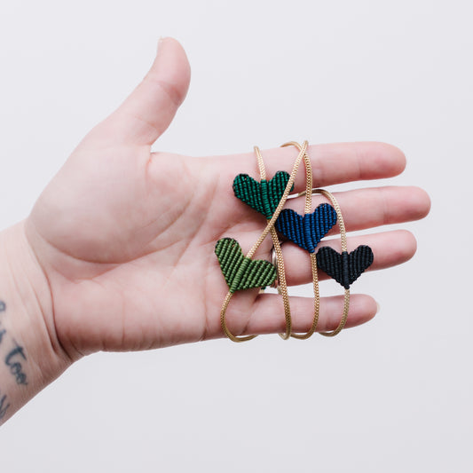 A collection of heart-shaped macrame bracelets in various colors, displayed on a hand.