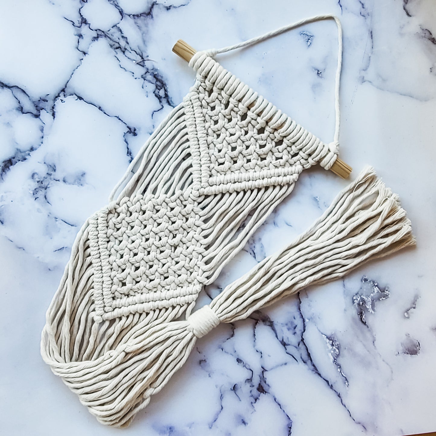 A macrame plant hanger in beige, laid out on a granite table
