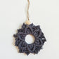 A charcoal colored macrame snowflake ornaments on a white background