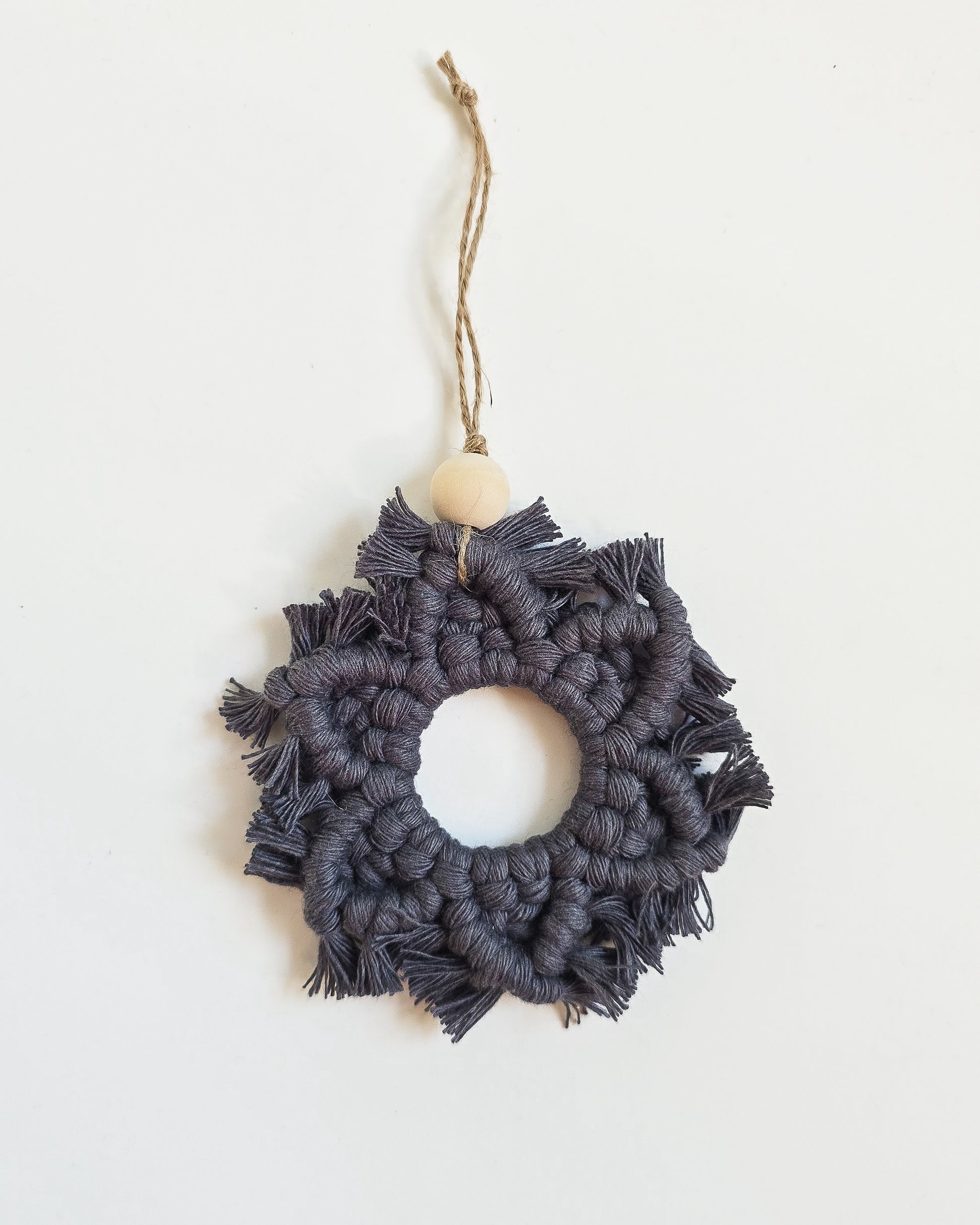 A charcoal colored macrame snowflake ornaments on a white background