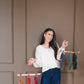 Woman holding a decorative hanging with colorful macrame feathers against a brown wall.