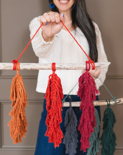Person holding a decorative item with red macrame feathers against a neutral background