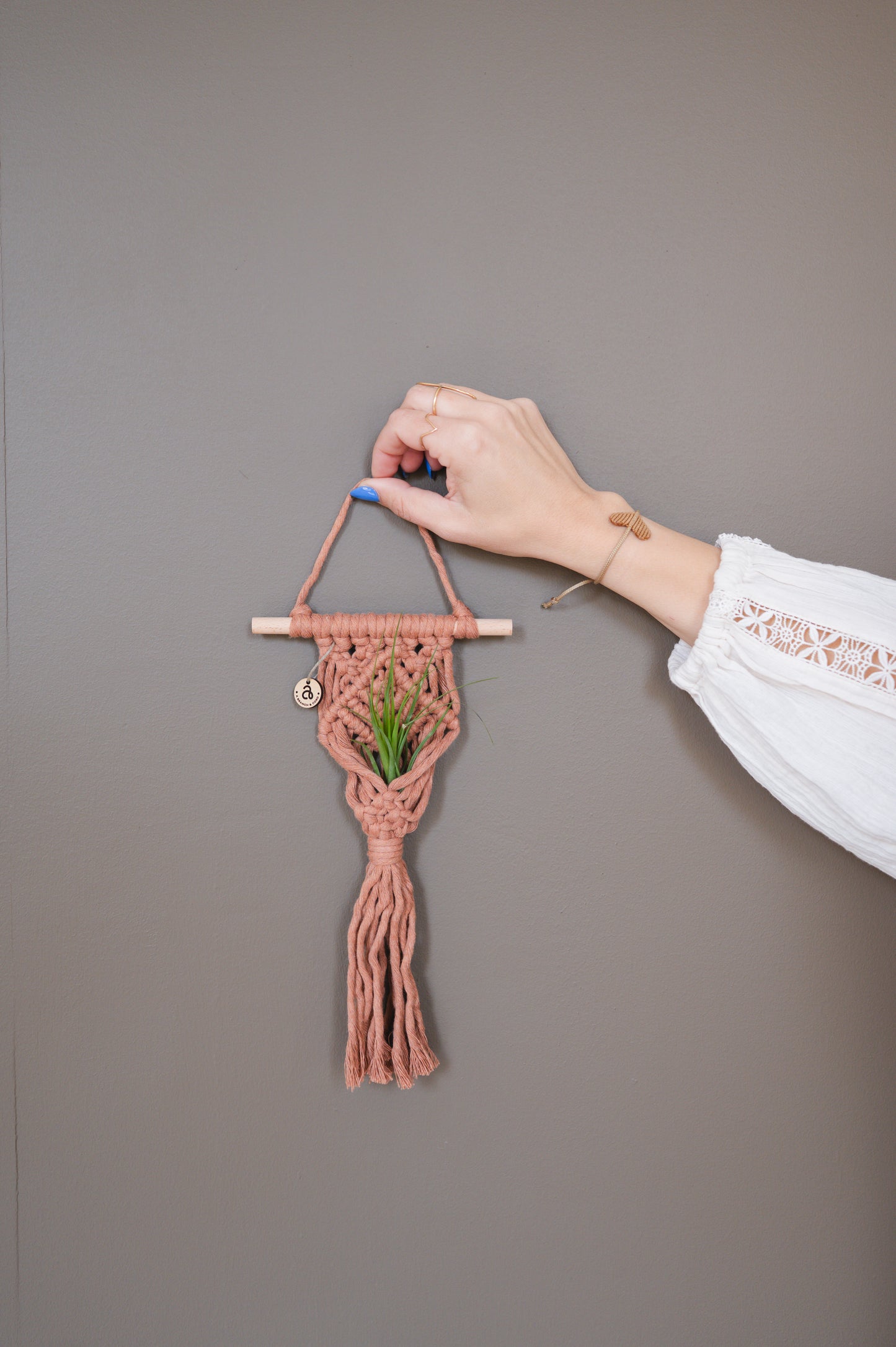 Hand holding a small woven wall hanging with a plant against a plain background