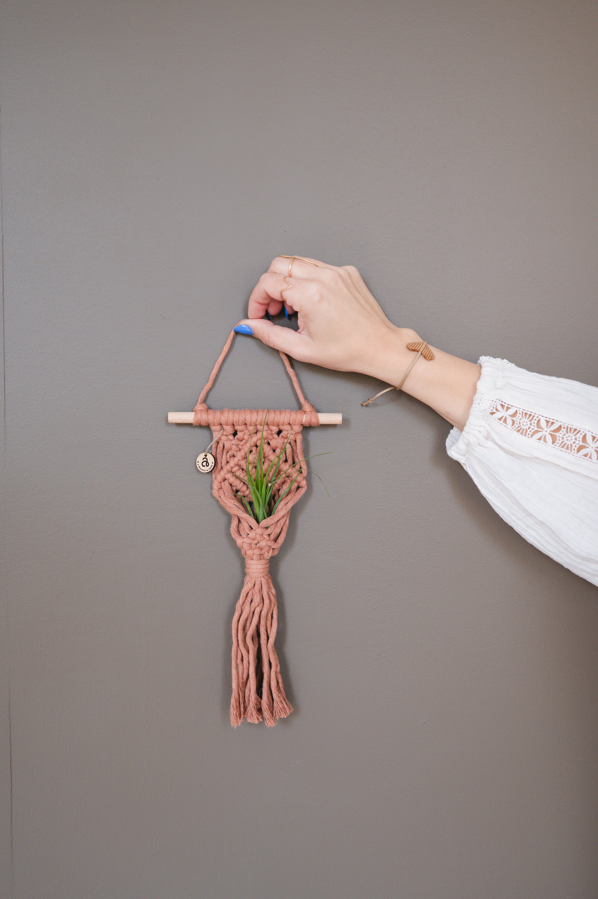 Hand holding a small woven wall hanging with a plant against a plain background